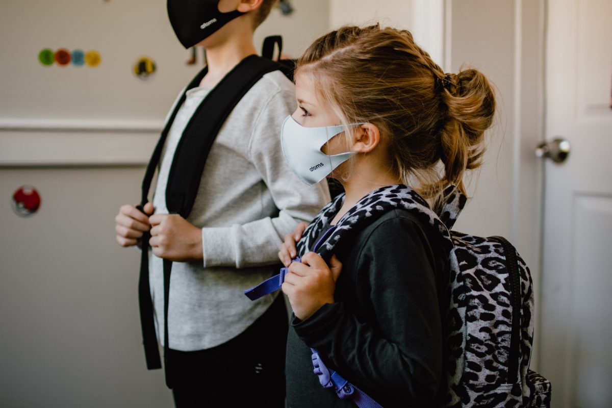 two children wearing face masks and carrying backpacks